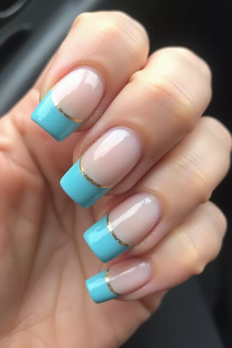 Aqua Tips With Gold Accents Close-up of a woman's hand with five fingers displaying aqua blue French tips with thin gold stripe separating the blue from the natural nail base, with high-shine finish.