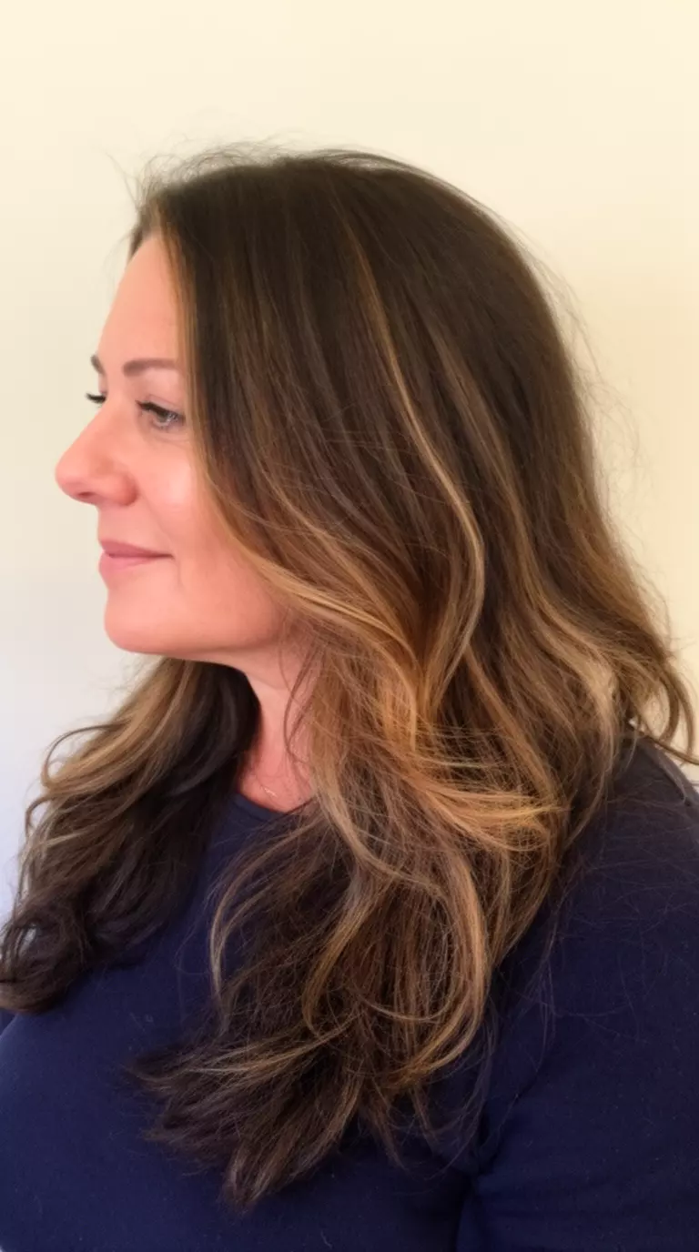 casual close-up photo of a 40-year-old woman wearing a dark top with a dark brown hair with lighter brown highlights colored long, wavy hairstyle, side profile view, minimal background