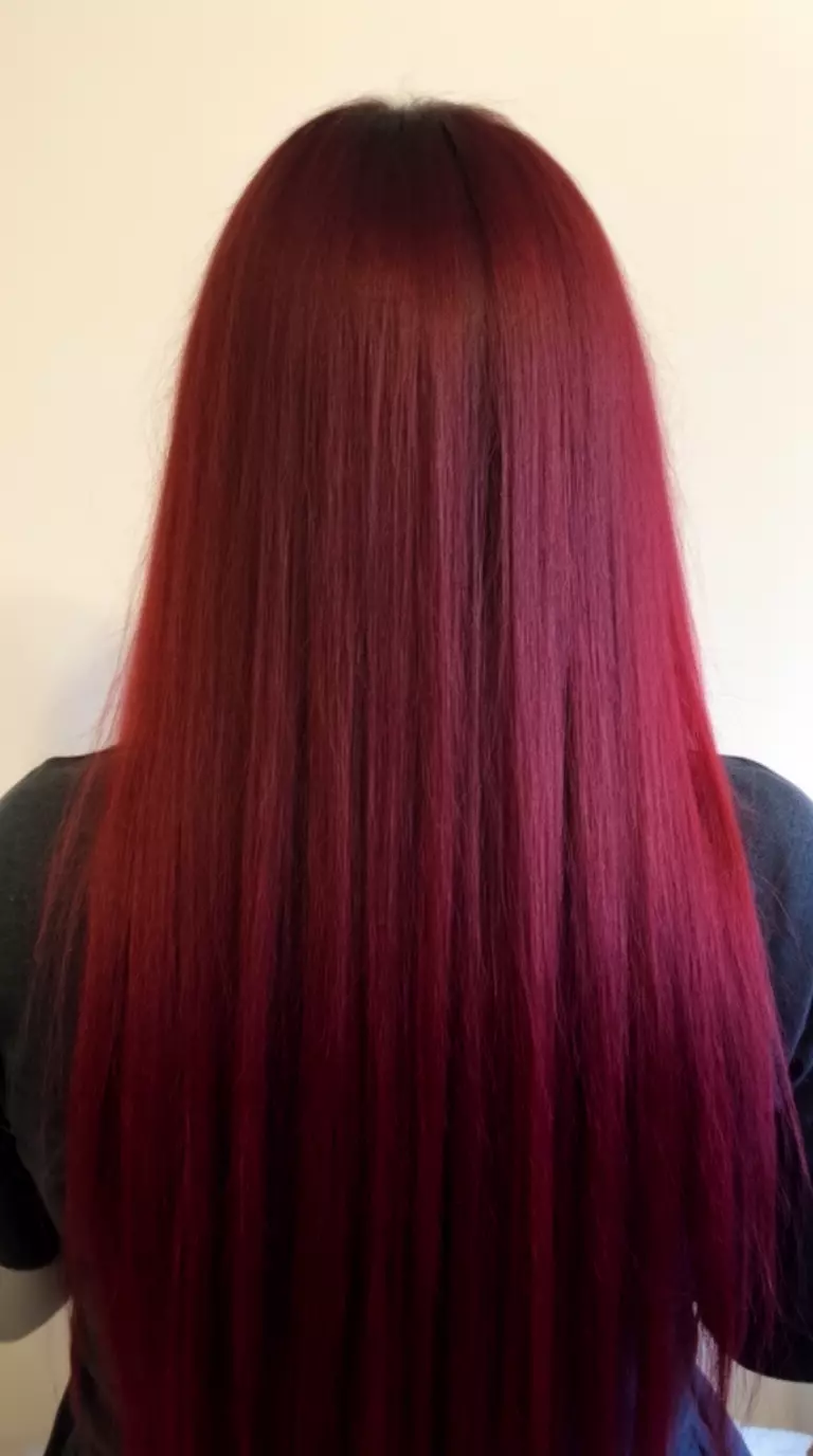 casual close-up photo of a 31-year-old woman wearing a dark top with a deep red/burgundy colored very long hairstyle, back view, minimal background