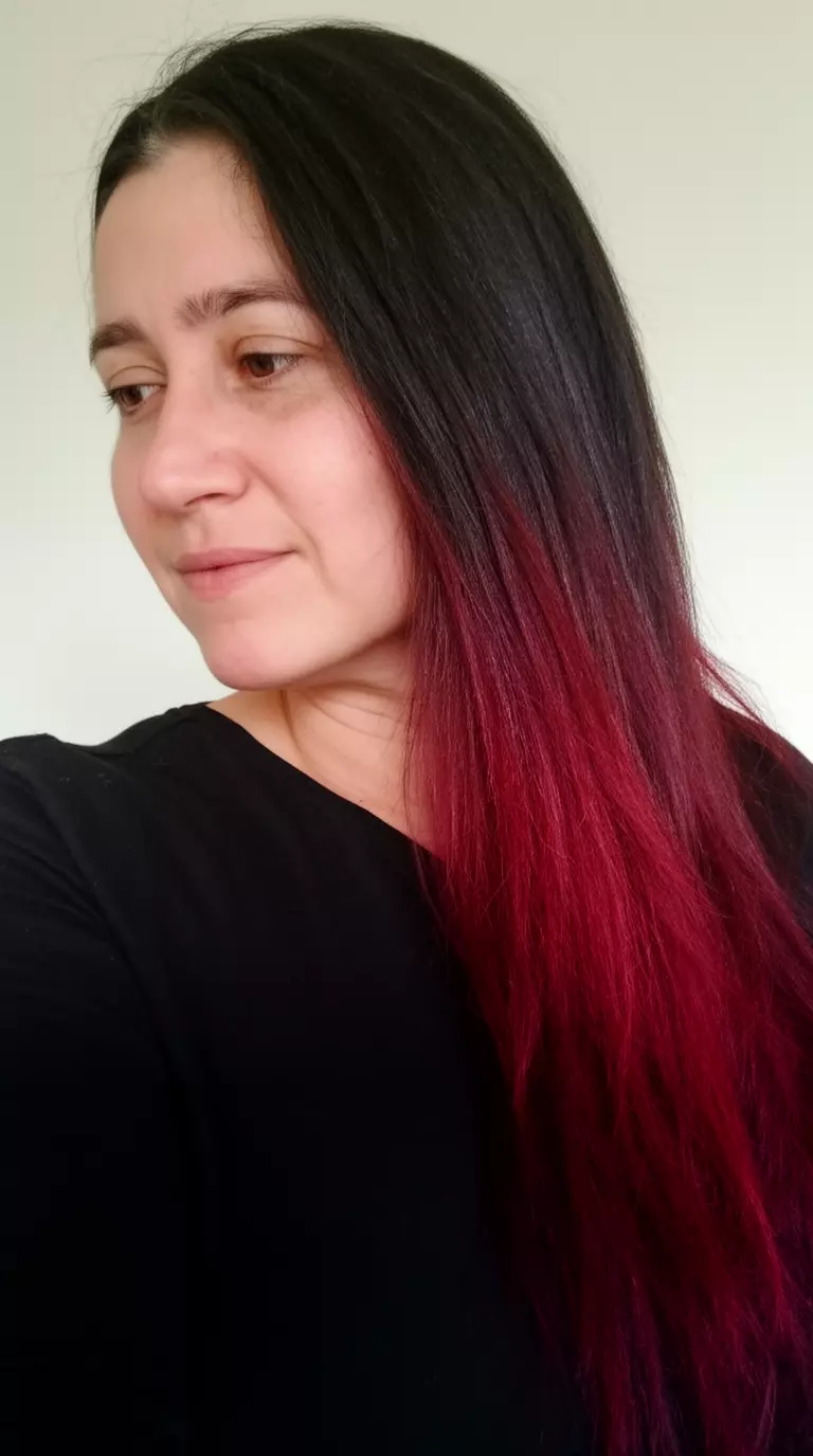 casual close-up photo of a 35-year-old woman wearing a black top with a dark hair with deep red/maroon ombre colored long hairstyle, side view, minimal background
