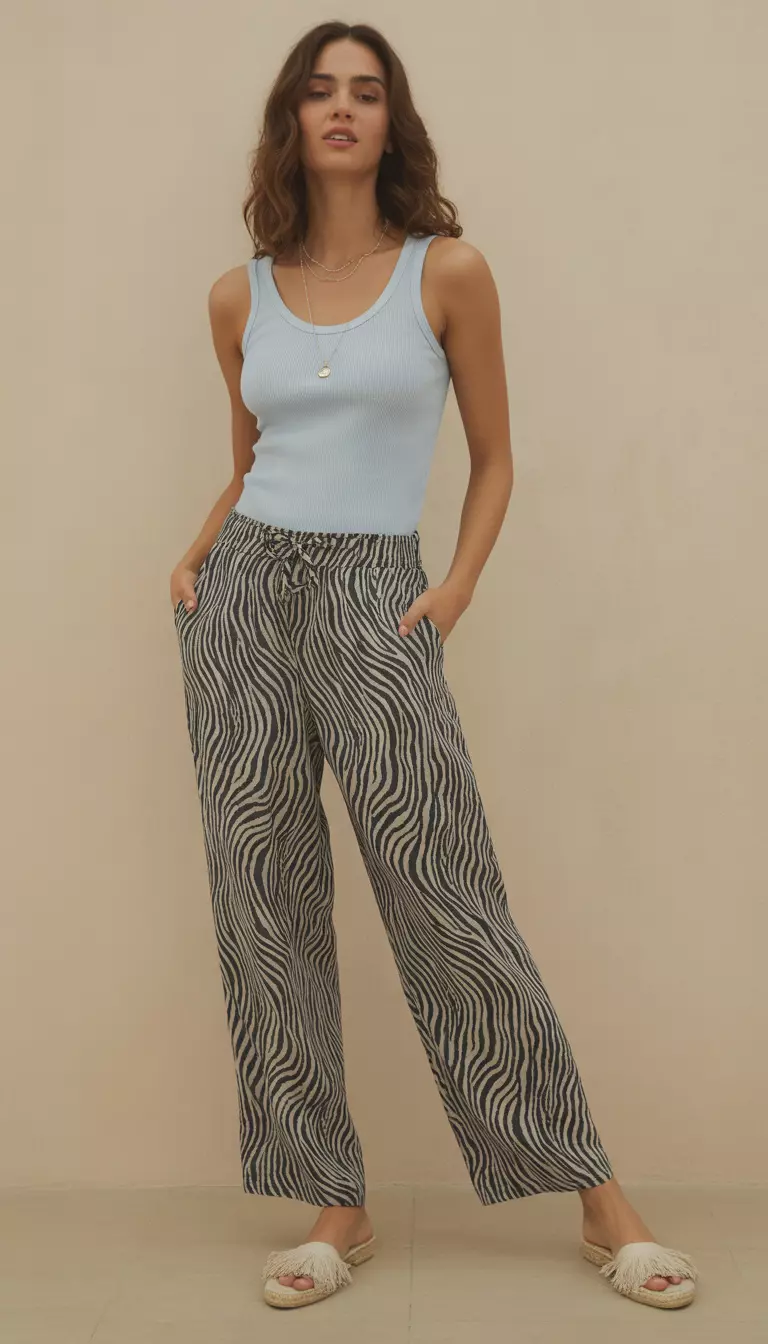 A beautiful woman in black and white zebra print linen beach pants, a baby blue tank top, and fringe espadrilles.