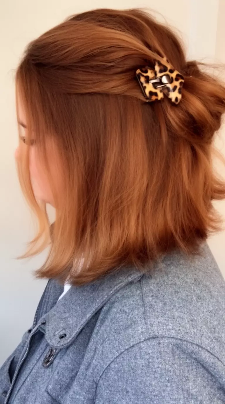 casual close-up photo of a 28-year-old woman wearing a gray jacket with a cocoa brown colored half up hairstyle with a leopard claw clip, back and side profile, minimal background