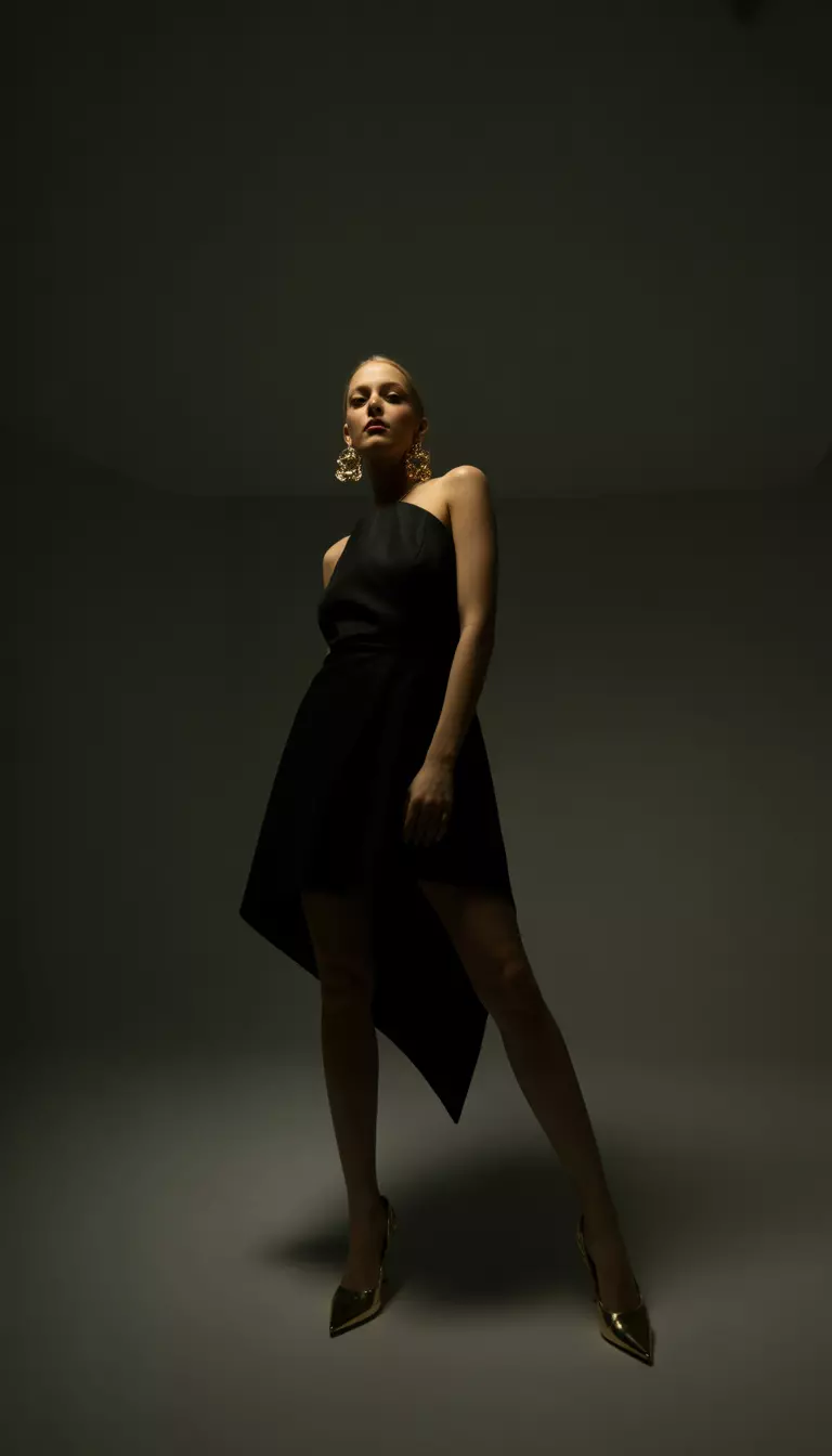 Asymmetrical Hem Black Dress A beautiful woman in a black dress with an uneven asymmetrical hem, gold stilettos, and large gold statement earrings.