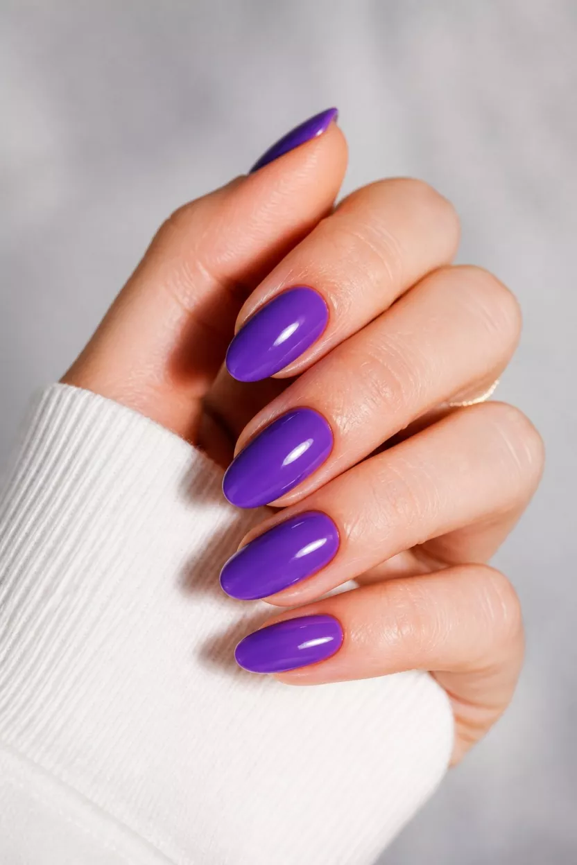 Vibrant Ultraviolet Purple close-up shot of a woman’s hand with five fingers showing nails with almond-shaped nails painted a rich, vibrant, glossy ultraviolet purple color