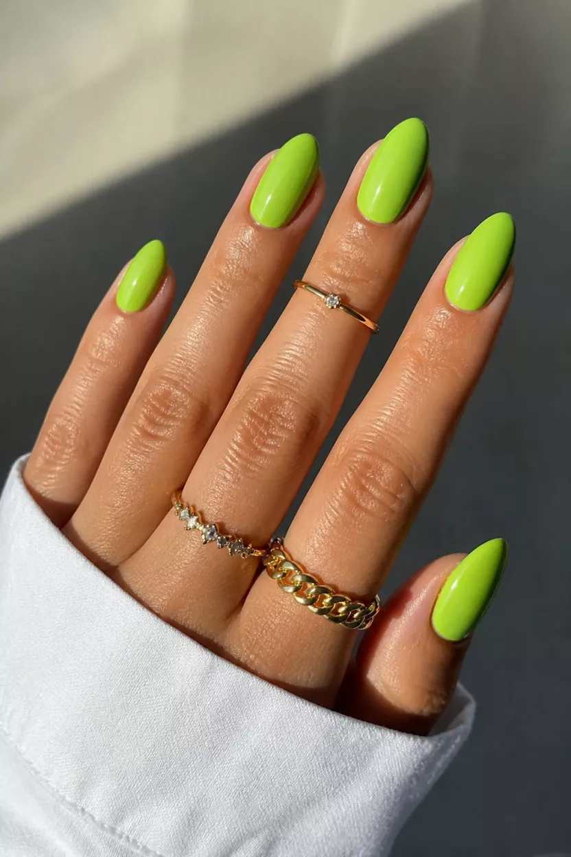 Vibrant Lime Green close-up shot of a woman’s hand with five fingers showing nails with ten almond-shaped nails painted a cheerful, vibrant lime green with delicate rings