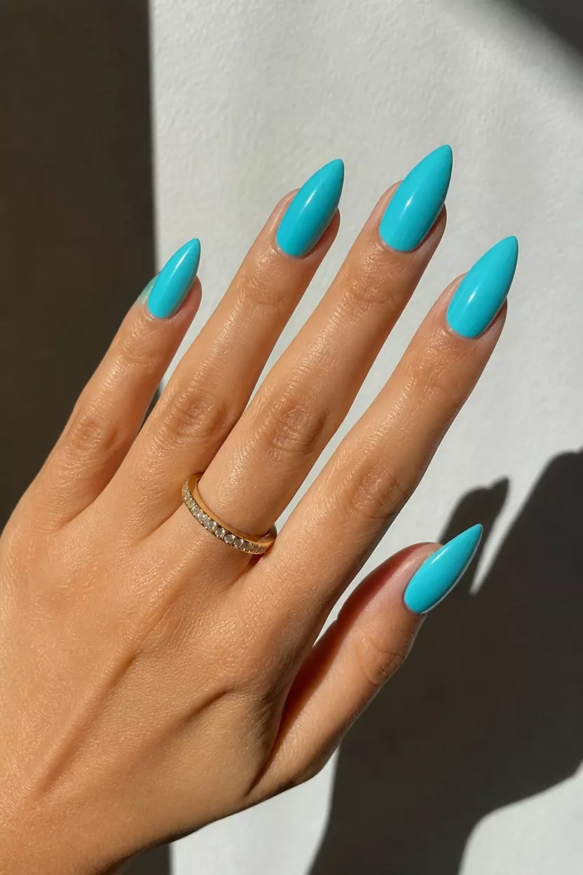 Vibrant Glinting Turquoise close-up shot of a woman’s hand with five fingers showing nails with long, pointed nails painted a vibrant, glossy turquoise blue highlighted by bright sunlight and sharp shadows