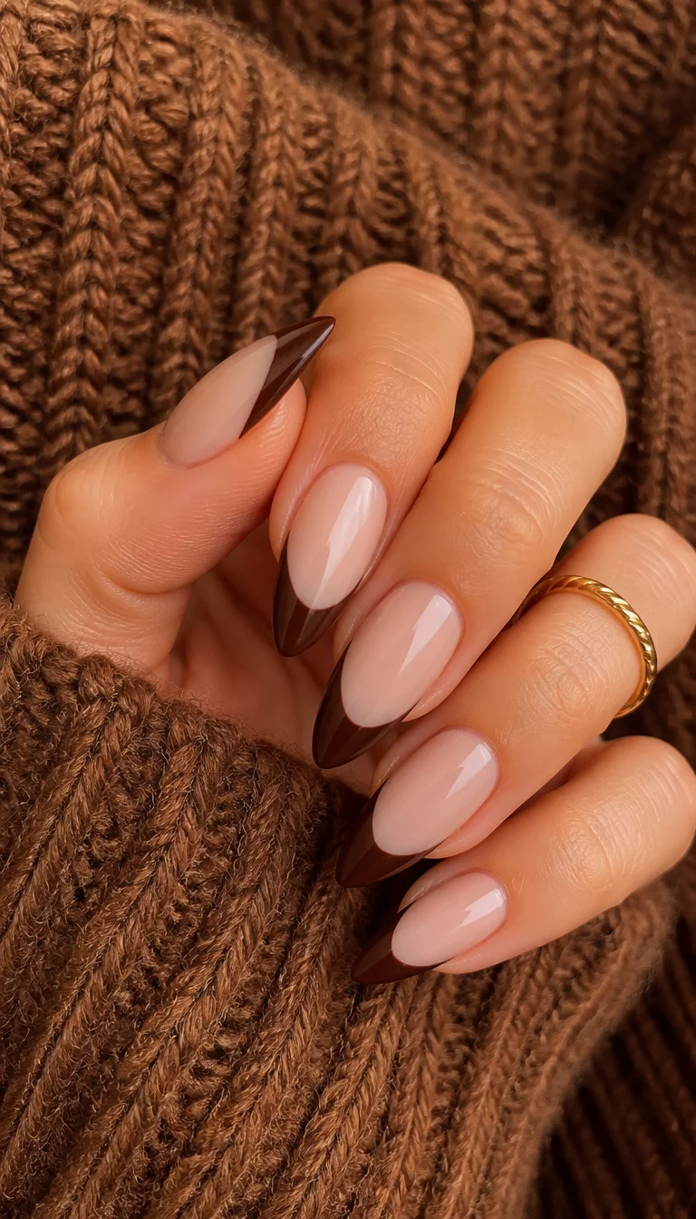 close-up shot of a woman’s hand with five fingers showing stiletto-shaped nails with a French tip in a deep brown color, warm textured knit sweater background.