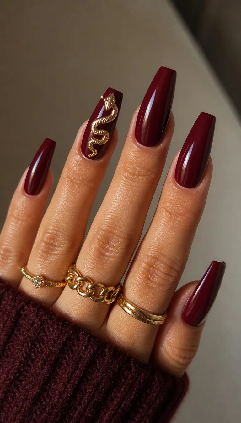 close-up shot of a woman’s hand with five fingers showing long deep red coffin shape nails, one accent nail featuring a shimmering 3D gold snake design, wearing several gold rings.