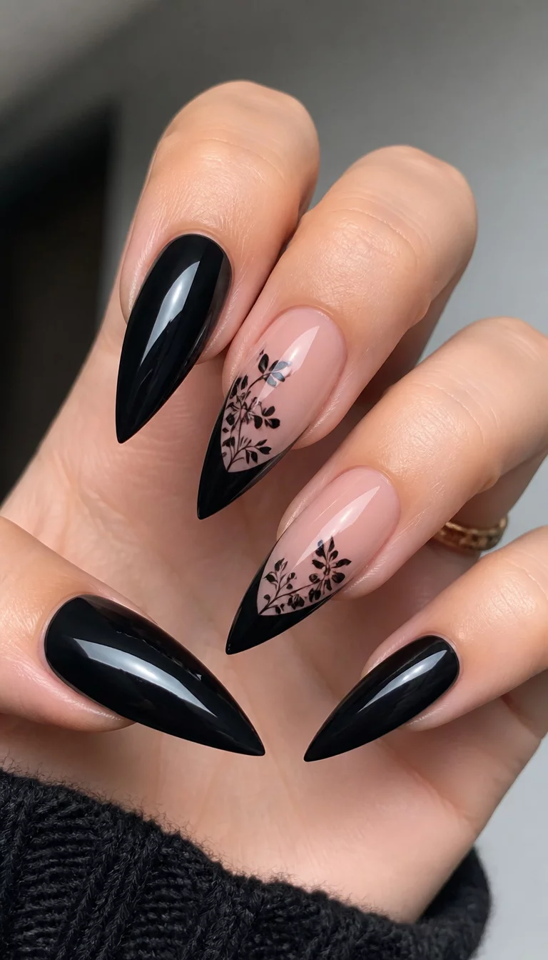 close-up shot of a woman’s hand with five fingers showing long, stiletto-shaped nails, some are glossy black, others feature a French tip with a dusky pink base and black floral designs.