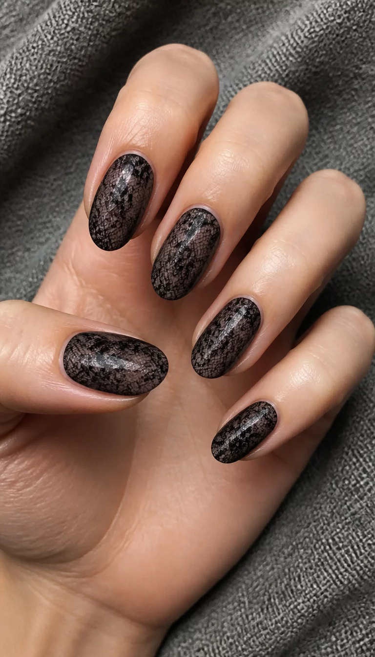 Black Lace Floral Patterns close-up shot of a woman’s hand with five fingers showing nails with oval-shaped nails with a sheer, lace-like black floral pattern over a greyish-black base, grey textured fabric background.
