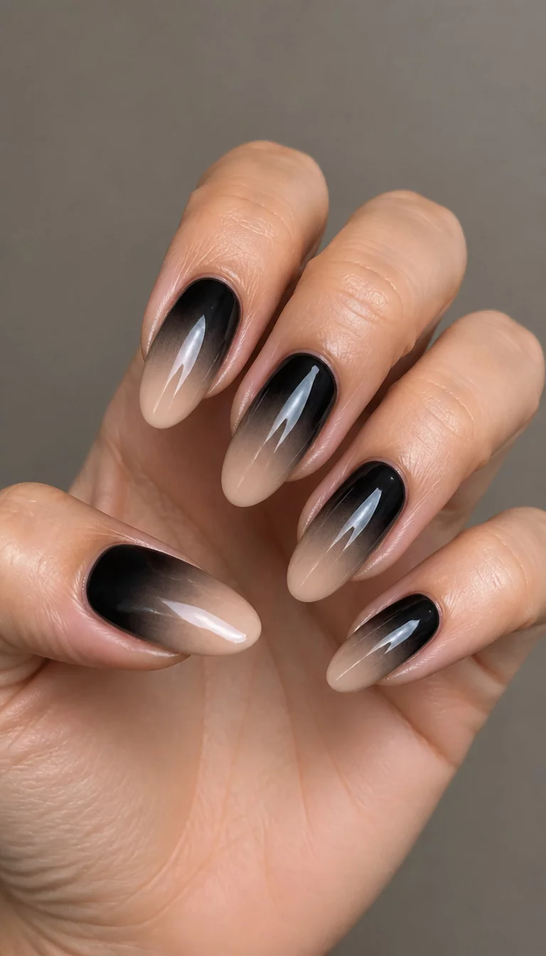 Natural To Black Fade close-up shot of a woman’s hand with five fingers showing nails with long, oval-shaped nails featuring a black to natural beige ombre design, neutral lighting background.