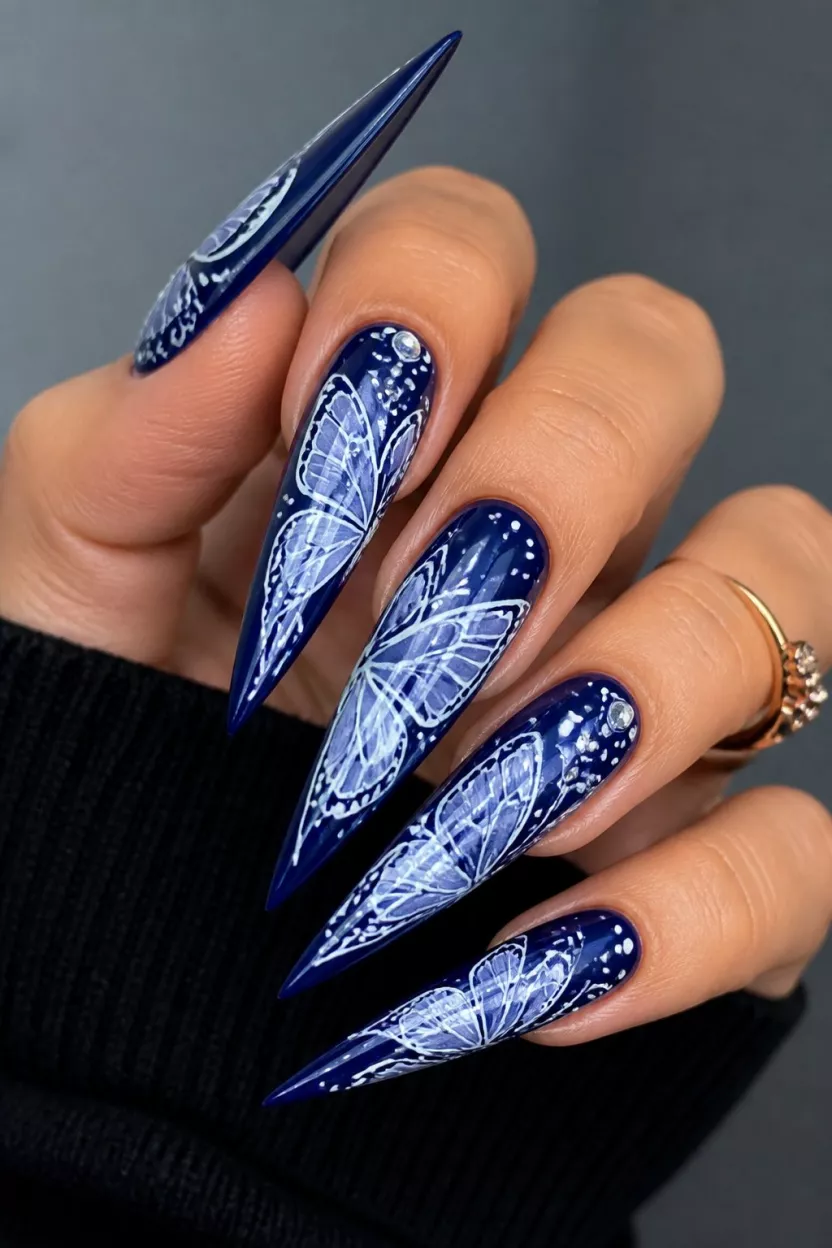 close-up shot of a woman’s hand with five fingers showing nails with very long dark blue stiletto nails with intricate white butterfly wing paintings