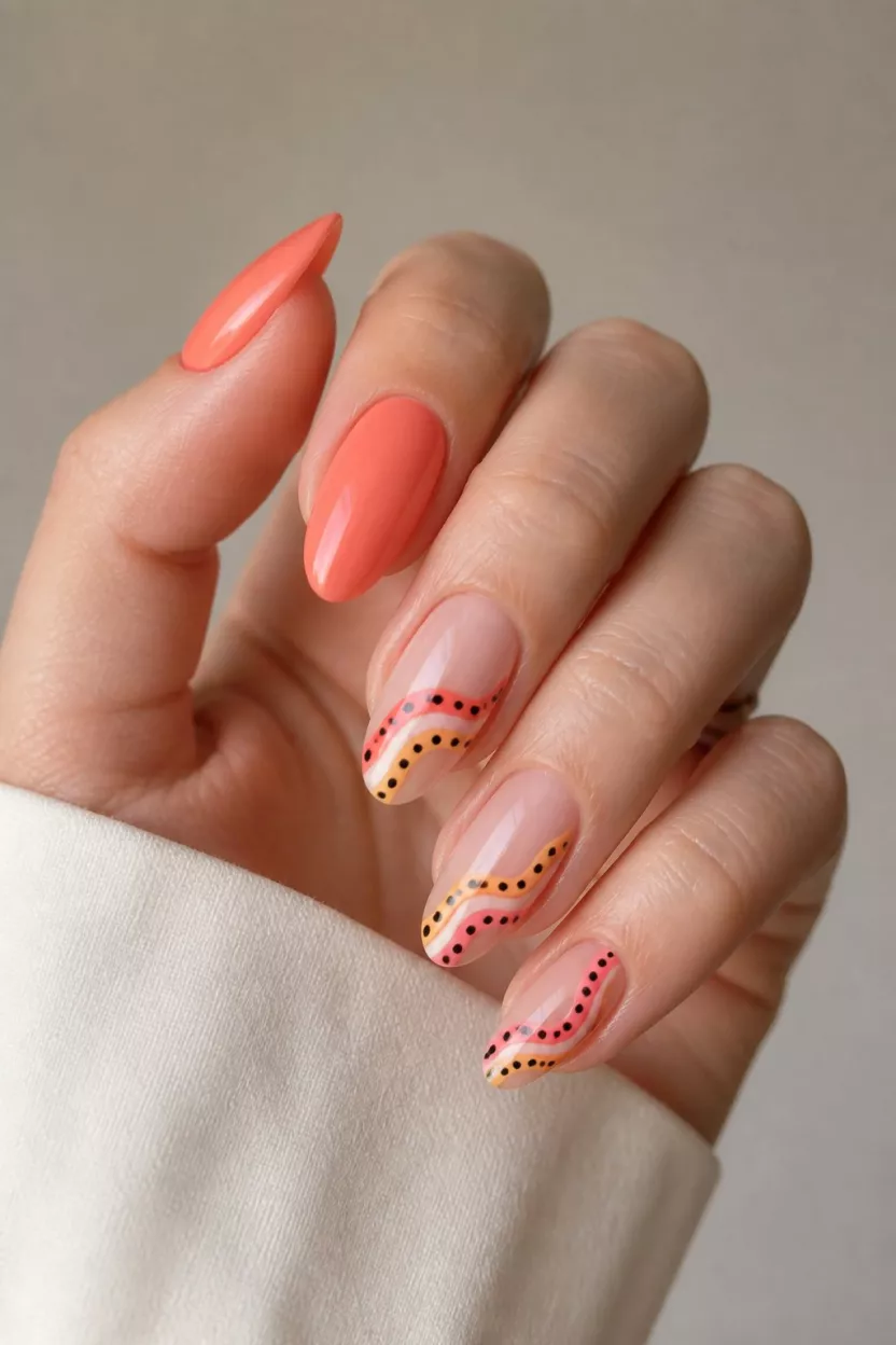 close-up shot of a woman’s hand with five fingers showing nails with almond nails featuring a mix of solid coral polish and sheer tips with curved pink, yellow, and red stripes and black polka dots, minimalist background.