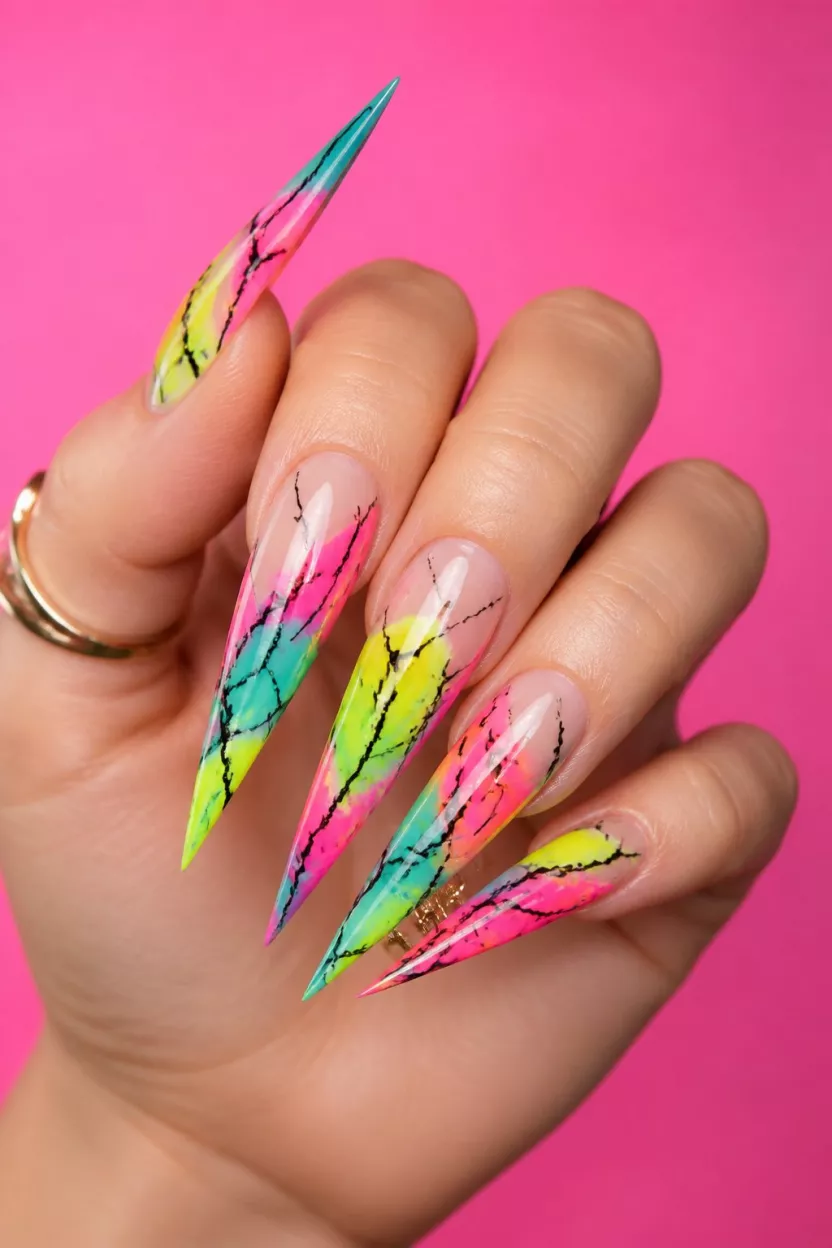 close-up shot of a woman’s hand with five fingers showing nails with extreme stiletto nails featuring vibrant neon pink, yellow, and teal abstract marbling with black crackle lines over a sheer base, bright backdrop.