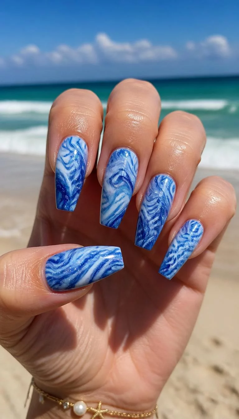 Ocean Wave Blue Marble close-up shot of a woman’s hand with five fingers showing nails with coffin nails with a mesmerizing blue and white marbled design, against a beachy background.