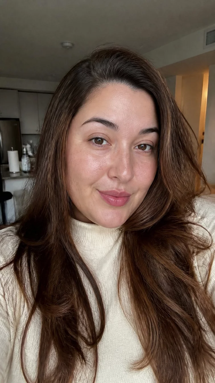 selfie of a 32-year-old Mediterranean woman with a oval face, fair, narrow nose, thin arched eyebrows, and full lips. Her face features small scar on the eyebrow, light freckles, and subtle natural facial asymmetry. She has monolid brown eyes, rounded cheeks, subtle smile, playful. She is plus-size and is wearing a cream mock neck sweater with reddish-tan cinnamon swirl espresso long layers hair, overcast daylight, indoor
