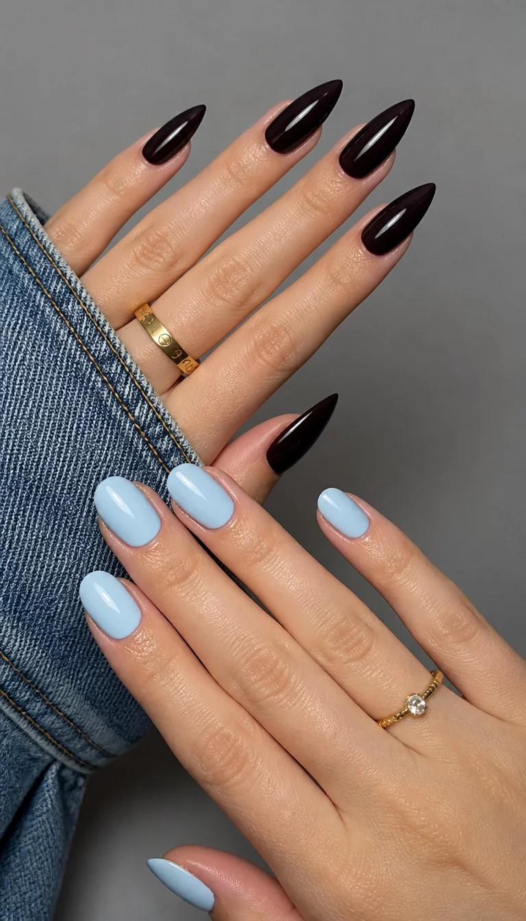 Mixed Texture Stilettos close-up shot of a woman’s hand with five fingers showing nails with elegant dark pointed stiletto nails and a hand with oval light blue nails, denim and plain grey background.