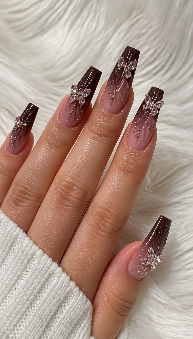 close-up shot of a woman’s hand with five fingers showing long, dark brown and pink ombre coffin nails enhanced with intricate ribbed details and butterfly-shaped rhinestones, soft white rug background