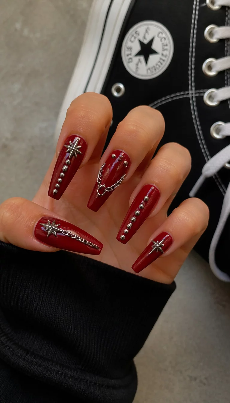 close-up shot of a woman’s hand with five fingers showing long, coffin-shaped nails in deep red with silver stud and chain embellishments, Converse sneakers background