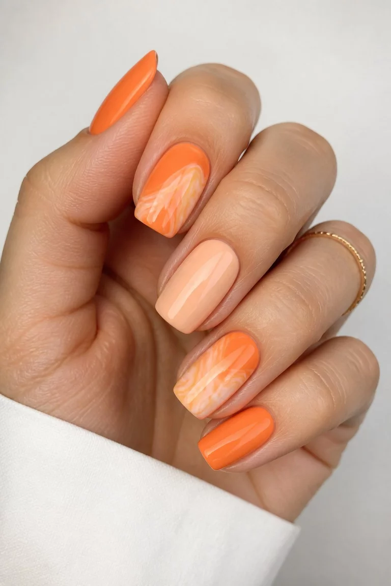 The Orange Marble Mix close-up shot of a woman’s hand with five fingers showing nails with a mix of square and oval shapes with solid orange marble swirl orange and white and pale peach colors.