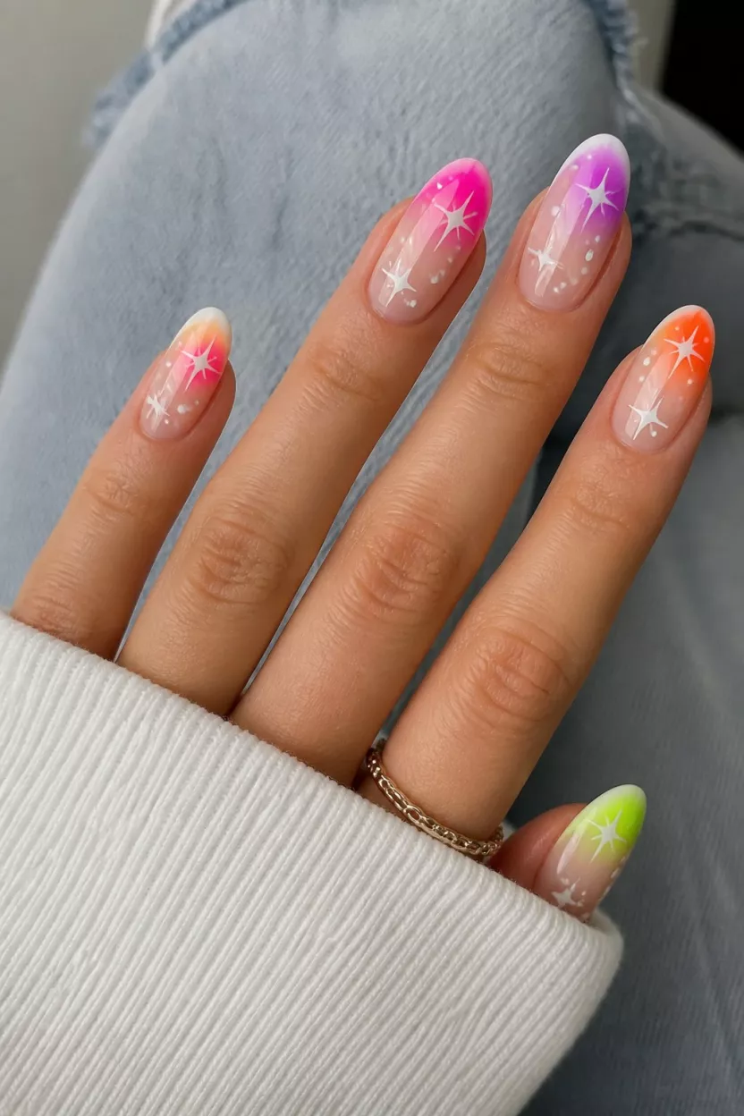 close-up shot of a woman’s hand with five fingers showing nails with oval nails featuring neon color blurs and ombre tips over a French base with stars and spots, casual clothing background.