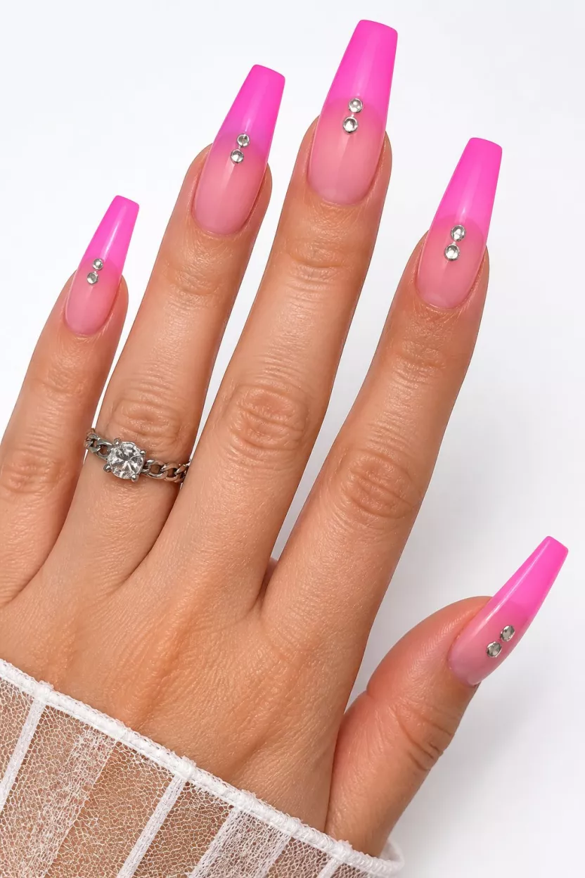 close-up shot of a woman’s hand with five fingers showing nails with long coffin-shaped nails with a neon pink to sheer fuchsia ombre and silver metal studs, white background.