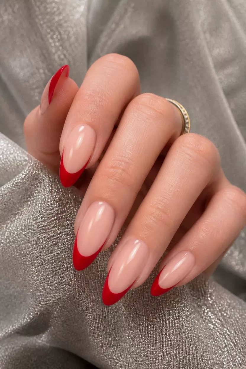 close-up shot of a woman’s hand with five fingers showing nails with long almond nails in a classic French manicure style with bold red tips, sheer base, sparkly fabric background.