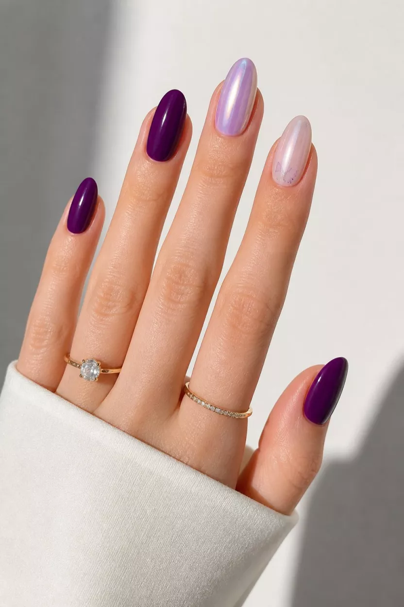 Purple Hues And Butterfly Decals close-up shot of a woman’s hand with five fingers showing dark purple short nails, iridescent lavender long nails, milky sheer nails, and butterfly decals, on a light background.