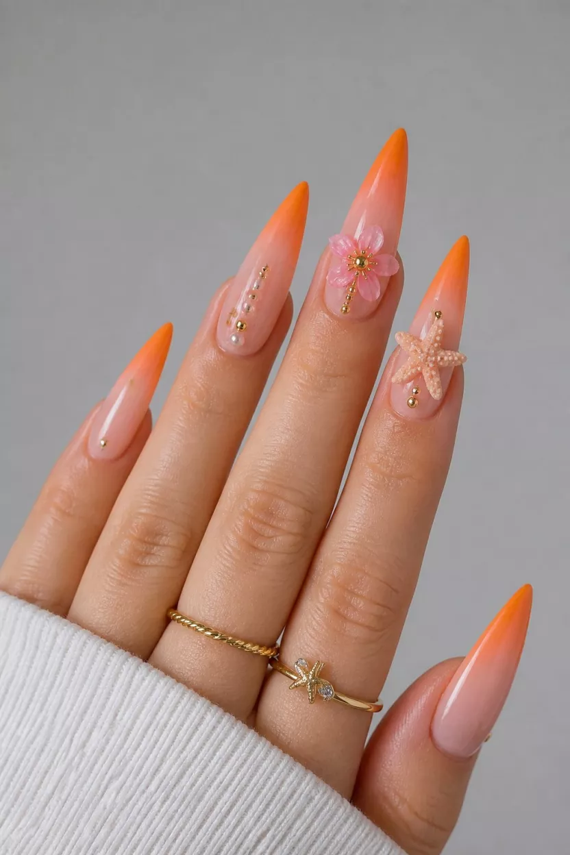 Sunset Ombre With 3D Charms close-up shot of a woman’s hand with five fingers showing long stiletto nails with a sheer base and vibrant orange ombre tips, decorated with a pink 3D flower and a 3D starfish, over a neutral background.