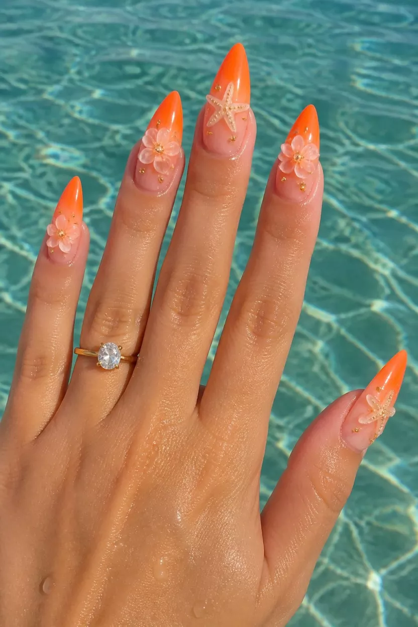 The Neon Ocean Ombre close-up shot of a woman’s hand with five fingers showing nails with long, sharp almond nails displaying a striking ombré effect fading from clear to bright neon orange tips, 3D flower and starfish embellishments, water background.