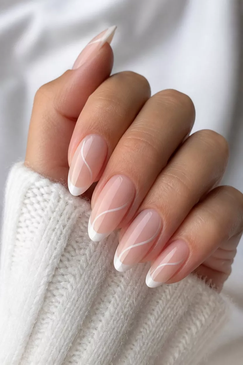 close-up shot of a woman’s hand with five fingers showing nails with almond-shaped nails displaying a clean modern French manicure style with swirling sheer white lines over a natural pink base, white knit fabric.