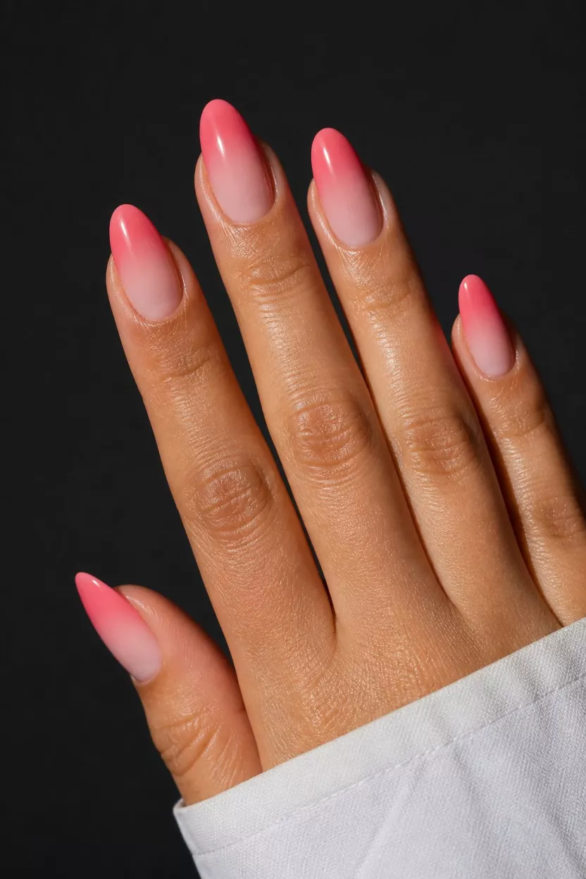 close-up shot of a woman’s hand with five fingers showing nails with almond-shaped nails display a warm coral pink ombré fade from sheer nude near the cuticle to a vibrant sunset hue at the tip, dramatic lighting.