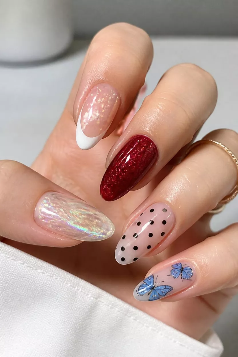Iridescent Butterfly Wings close-up shot of a woman’s hand with five fingers showing nails with iridescent, abstract art, classic French tips, deep red glitter, polka dots, and light blue butterfly designs.