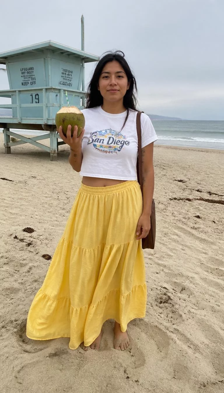 Graphic Crop Tee and Yellow Tiered Skirt A photorealistic full body shot of a 34-year-old Latina woman with a oval face, deep brown, rounded nose, thick natural eyebrows, and wide lips. Her face features gap between front teeth, faint under-eye shadows, and subtle natural facial asymmetry. She has monolid dark brown eyes, high cheekbones, neutral expression, playful. She is petite with dark hair hair and is wearing a white graphic crop tee and a long yellow tiered skirt, holding a coconut and brown purse, sandy beach with a lifeguard station, no people in the background, high-quality mobile photography, shot on an iPhone 14.