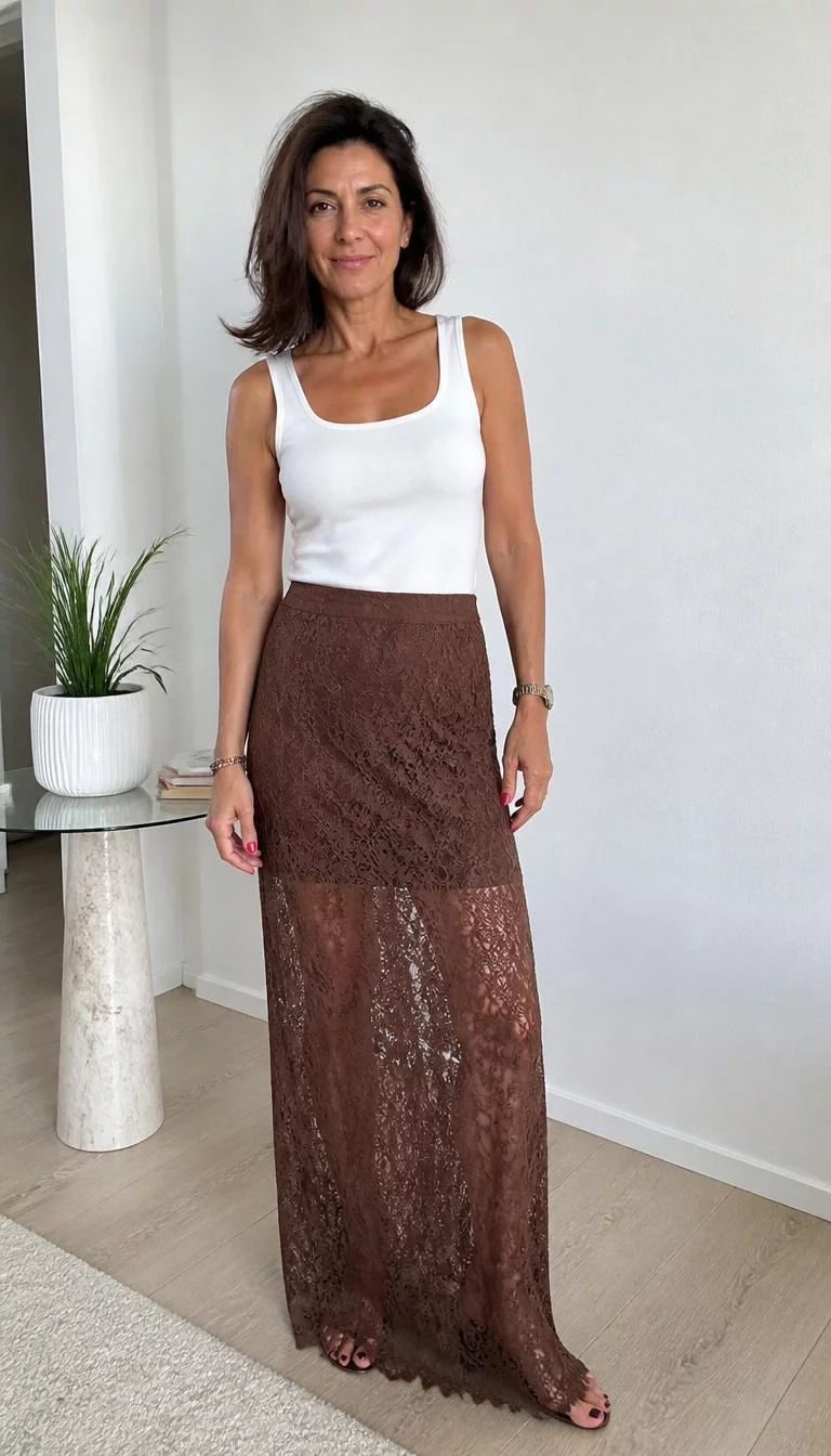 White Tank Top and Brown Lace Maxi Skirt A photorealistic full body shot of a 47-year-old Southern European woman with a oval face, deep brown, rounded nose, softly curved eyebrows, and heart-shaped lips. Her face features small scar on the eyebrow, faint under-eye shadows, and subtle natural facial asymmetry. She has deep-set gray eyes, rounded cheeks, subtle smile, confident. She is average build with dark brown shoulder-length blowout hair and is wearing a white tank top, brown lace maxi skirt, standing in a brightly lit indoor space, no people in the background, high-quality mobile photography, shot on an iPhone 14.
