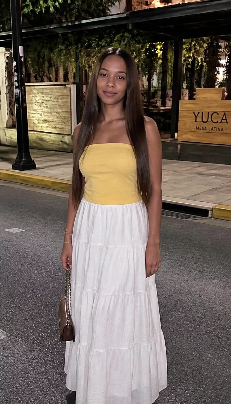 Yellow Tube Top and White Tiered Maxi Skirt A photorealistic full body shot of a 28-year-old Afro-Caribbean woman with a oblong face, deep brown, straight nose, straight eyebrows, and heart-shaped lips. Her face features uneven eyebrows, subtle acne marks, and subtle natural facial asymmetry. She has round brown eyes, high cheekbones, closed-mouth smile, relaxed. She is average build with long brown blowout hair and is wearing a yellow tube top, white tiered maxi skirt, standing on a street outside a restaurant, no people in the background, high-quality mobile photography, shot on an iPhone 14.