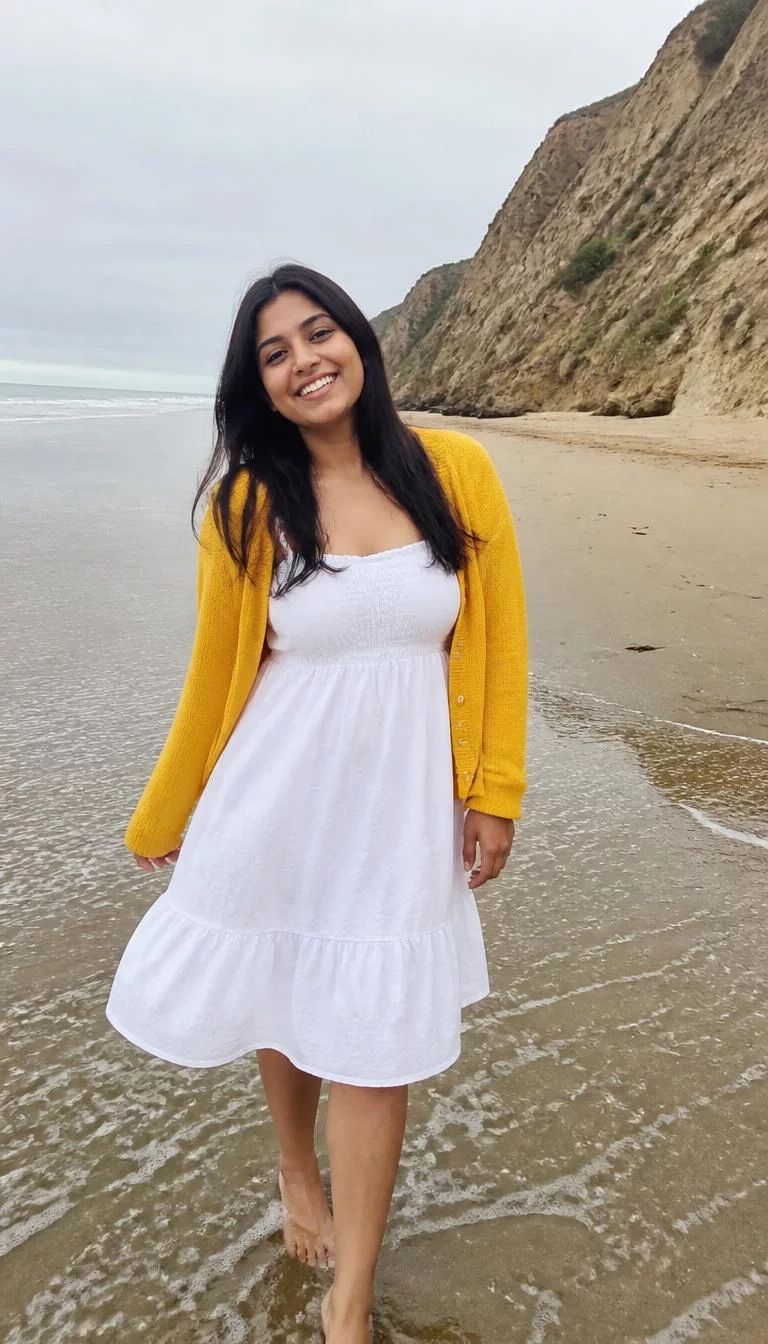 Classic White Summer Dress And Yellow Accessories A photorealistic full body shot of a 26-year-old South Asian woman with a round face, golden brown, straight nose, feathered eyebrows, and wide lips. Her face features gap between front teeth, a few laugh lines, and subtle natural facial asymmetry. She has downturned amber eyes, high cheekbones, broad smile, playful. She is curvy build with black long hair and is wearing a white cotton sundress and a yellow cardigan, beach scene with sand and cliffs, no people in the background, high-quality mobile photography, shot on an iPhone 14.