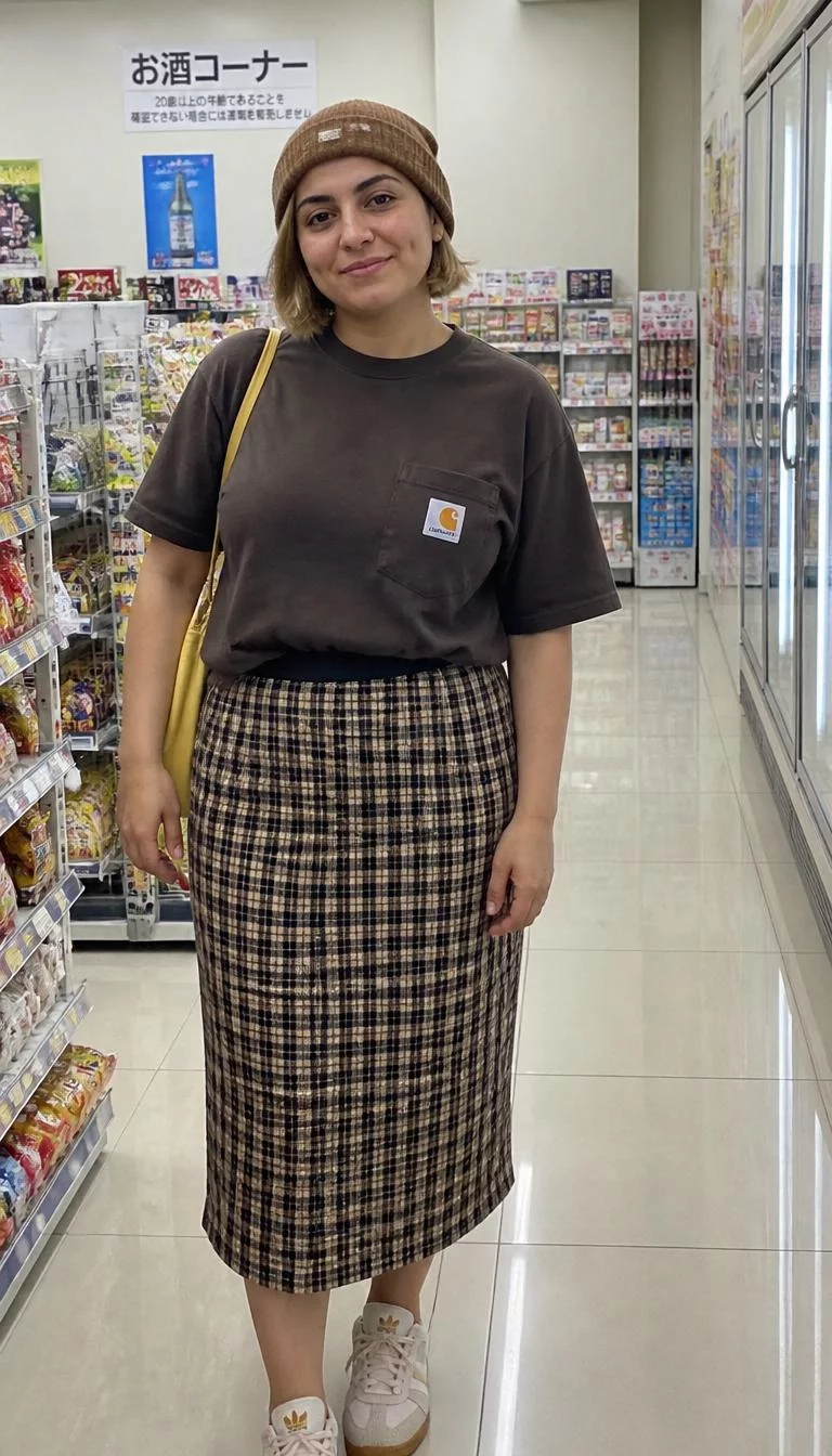 Graphic T-Shirt and Checkered Midi Skirt A photorealistic full body shot of a 32-year-old Middle Eastern woman with a diamond face, olive, straight nose, thin arched eyebrows, and thin lips. Her face features dimples, faint under-eye shadows, and subtle natural facial asymmetry. She has upturned amber eyes, rounded cheeks, subtle smile, cheerful. She is curvy build with blonde hair in a bob hairstyle hair and is wearing a brown bobble cap, Carhartt t-shirt, and checkered midi skirt, she carries a yellow bag, in a Japanese convenience store, no people in the background, high-quality mobile photography, shot on an iPhone 14.